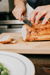 A person is cutting a piece of meat on a wooden cutting board. The meat is a whole chicken