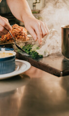 A person is cooking food on a stove with a pot of boiling water and a plate of greens