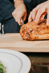 A person is cutting a piece of meat on a wooden cutting board. The meat is sliced into thin pieces