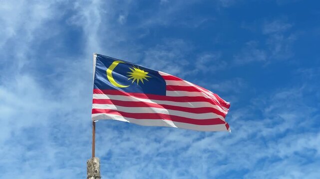 Malaysian Flag Waving in the Wind Against Blue Sky