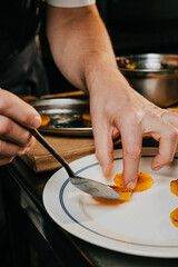 A man is preparing food on a plate with a fork. The plate has a few slices of orange on it