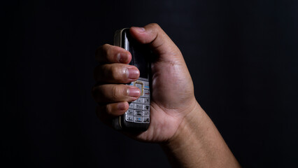 A person holding an old mobile phone vertically, framed in low-key lighting that reveals the device?s aged keypad and compact design. Suitable for retro tech concepts.