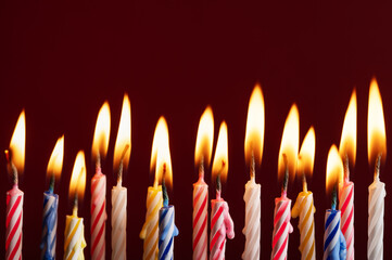 Row of colorful burning birthday candles on red background. Bright flames and vibrant colors with space for text or graphic elements. Ideal for celebration concepts.