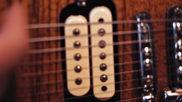 Close-up of guitar's body with strings, pickups, and wood grain. A hand is blurry in the corner