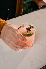 A man is holding a glass of pink drink with a lime wedge and a cinnamon stick in it