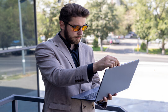 A man wearing a suit jacket and sunglasses is using a laptop outdoors