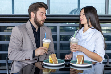 A man and a woman are sitting at a table in a cafe, holding drinks