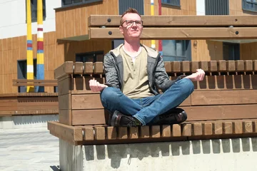 Fotobehang Lotusbloem A young European man relaxes in the lotus position on a wooden bench  © Alex