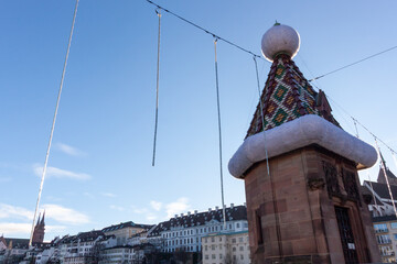 A decorative turret on a bridge over the Rhine River in Basel, adorned with a large Santa hat for the Christmas season, with the cityscape in the background