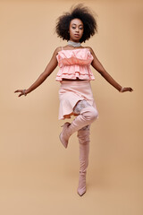 Curly young woman showcases stylish pink attire in a trendy studio setting