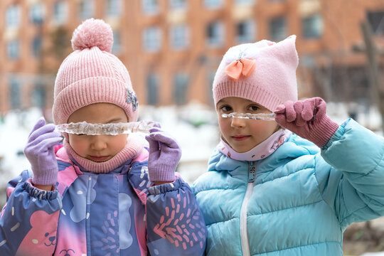 Happy girls look through icicles in winter snowy playground outdoors. Little children walk in winter - Powered by Adobe