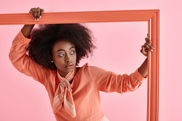 Curly young woman in stylish pink outfit poses creatively in studio