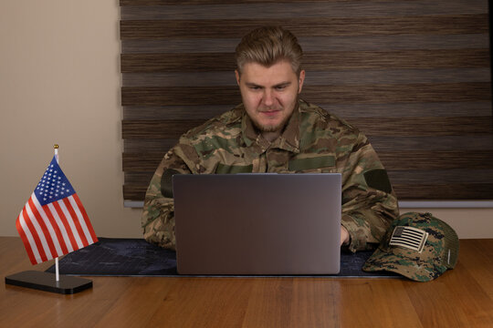 A service member is actively engaged in work on a laptop computer while seated