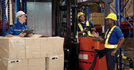 caucasian warehouse supervisor using clipboard checking inventory status near wrapped pallet while communicating with team during shipment preparation inside logistic stock facility - Powered by Adobe