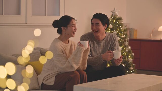 白熱灯のような夜の黄色い灯りの部屋で過ごすかわいいカップルのクリスマスツリーと冬　テレビなどメディアを見る