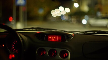 Blurry or bokeh street and car tail lights through a stationary car's windshield at night in the city. Stopped at the red traffic light, blurry cars driving across, unrecognizable male driver - Powered by Adobe