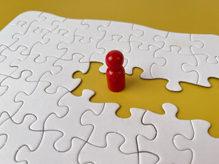 Red pawn or wooden figure standing in missing puzzle piece space on yellow background, symbolizing individuality, leadership, and uniqueness.