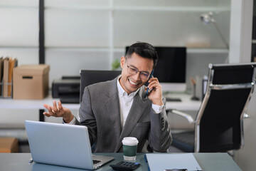 Businessman using smartphone and laptop computer in office. Happy man, entrepreneur, small business owner working online.