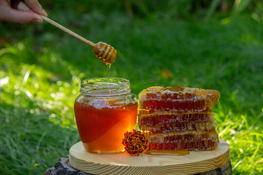 Natural honey dripping from a wooden dipper into a glass jar against a floral background