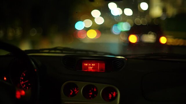 Blurry or bokeh street and car tail lights through a car's windshield driving at night in the city. Unrecognizable male driver,  rain drops on the windshield, real time video