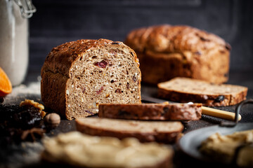 Rustic Christmas fruit bread filled with dried fruit, nuts and seeds, sliced and served on a dark textured surface. Ideal for festive, winter and holiday baking themes.