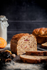 Rustic Christmas fruit bread filled with dried fruit, nuts and seeds, sliced and served on a dark textured surface. Ideal for festive, winter and holiday baking themes.