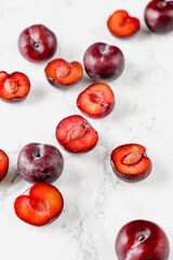 Fresh whole and halved red plums arranged on marble and dark surfaces, with optional spices and cutting board elements. Ideal for food styling, seasonal fruit themes and recipe content.