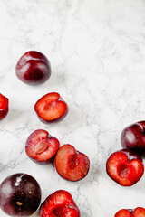 Fresh whole and halved red plums arranged on marble and dark surfaces, with optional spices and cutting board elements. Ideal for food styling, seasonal fruit themes and recipe content.