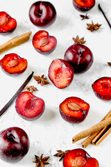Fresh whole and halved red plums arranged on marble and dark surfaces, with optional spices and cutting board elements. Ideal for food styling, seasonal fruit themes and recipe content.