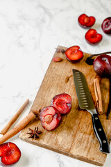Fresh whole and halved red plums arranged on marble and dark surfaces, with optional spices and cutting board elements. Ideal for food styling, seasonal fruit themes and recipe content.