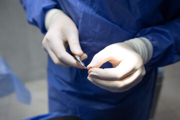 The doctor is holding a medical needle and surgical instruments, suturing a patient's wound in the...