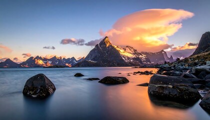 Scenic mountain range reflecting on calm water during sunset with orange-pink sky hues and rocky foreground