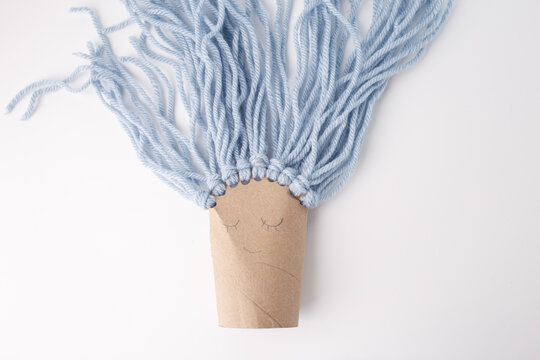 Handmade cardboard character with blue yarn hair, peaceful face expression, ideal for kids crafts, DIY blogs, educational content, toy branding, creative workshops, parenting media