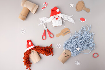 DIY kids craft project with cardboard dolls and yarn materials on grey background, useful for education business, craft supply stores, kids activity services, winter and Christmas workshops promotion
