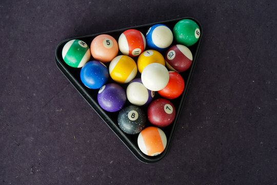 Close-up of colorful billiard balls numbered 1 to 15 arranged in a triangular rack on a dark purple pool table, ready for gameplay.