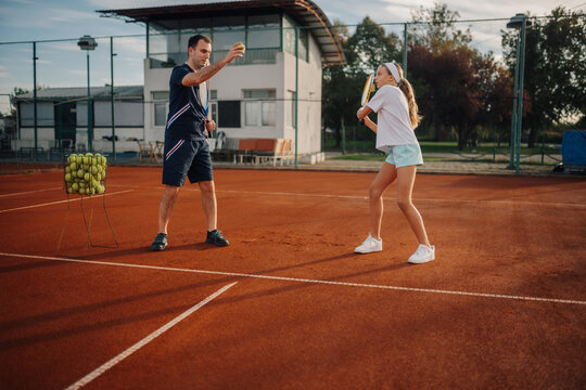 Tennis coach training girl on clay court - Powered by Adobe