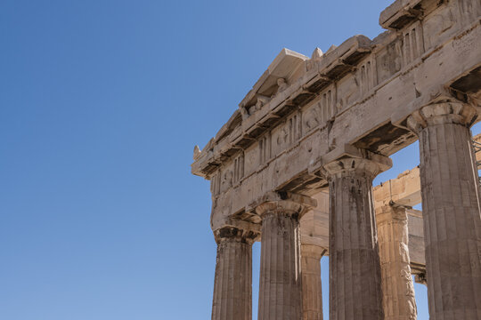 Detailed view of Parthenon frieze and corner columns in Athens. Detailed perspective of the Parthenon's corner showing carved friezes and robust Doric columns under bright sunlight.