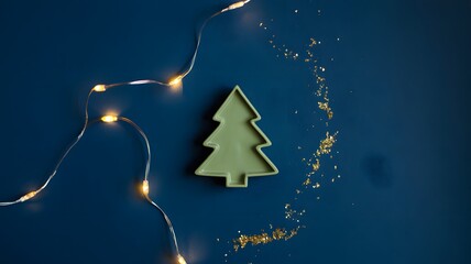 Green christmas tree decoration with fairy lights and golden glitter on a dark blue background, festive holiday concept