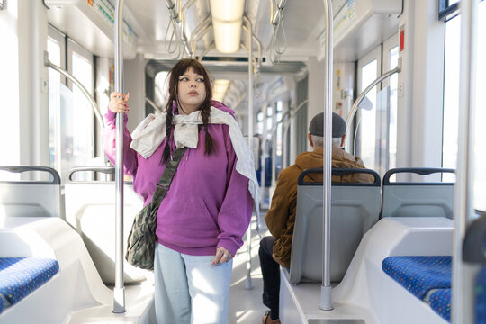 Young woman commuting on public transport holding pole - Powered by Adobe