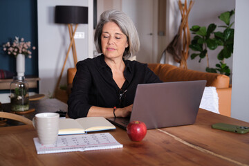 Focused mature woman using laptop, working remotely from home office