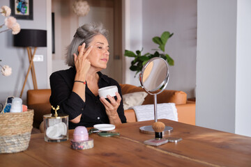 Mature woman taking care of her skin applying anti aging cream looking in the mirror