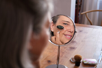 Mature woman improving her skin condition using a jade roller for a facial massage at home