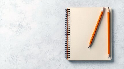 A blank spiral-bound notebook with two sharpened pencils resting on its pages, set against a textured, light-colored surface. The image is viewed from directly