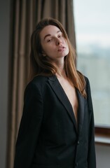 Fototapeta premium Portrait of a confident woman in a stylish, open blazer captured indoors with natural light streaming through the window
