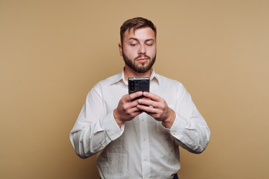 Young man using smartphone while wearing a white shirt in front of a neutral background during indoor setting - Powered by Adobe