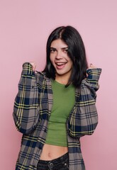 Girl in plaid shirt smiles and poses confidently against a pink background during a photoshoot