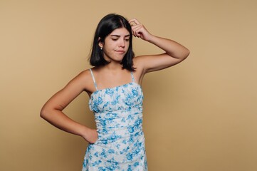 Obraz premium Young woman in blue floral dress with thoughtful expression against solid background