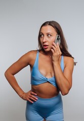 Naklejka premium Woman in blue athletic wear talking on the phone with a surprised expression in a studio setting