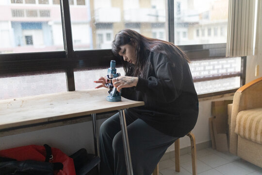 Young person studying with microscope at home table