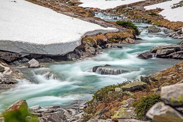 Turquoise alpine river cascading over rocks in snowy valley